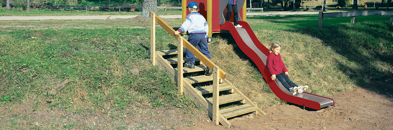 A child goes up terrain stairs to get to an embankment slide at a playground.